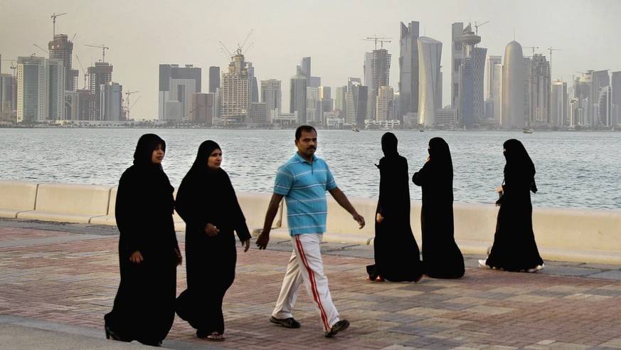 FILE- Qatari women and a man walk in front of the city skyline in Doha, Qatar, Saturday, April 7, 2012. The foreign fans descending on Doha for the 2022 FIFA World Cup will find a country where women  ...
