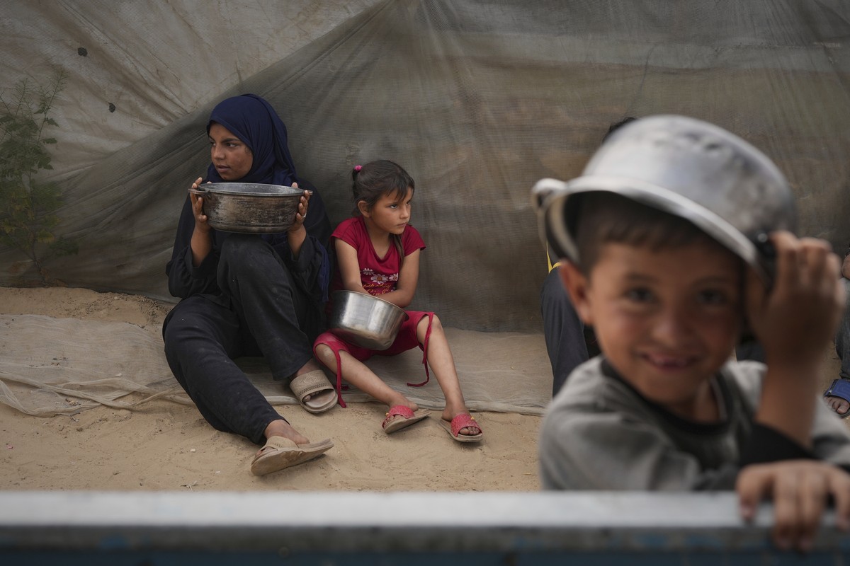 Raghad and her younger sister Mira hold on to their cooking pots as they wait to fill them with food, in Muwasi, on the outskirts of Khan Younis, in the southern Gaza Strip, April 24, 2025. (AP Photo/ ...