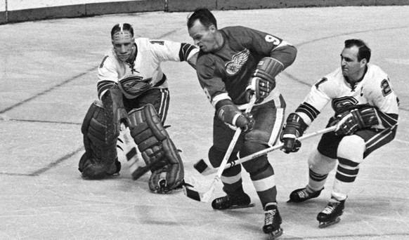In this Oct. 26, 1967 photo California Seals goalie Charlie Hodge, left, knocks the puck away as Detroit Red Wings&#039; star Gordie Howe tries a shot on goal as the Seals&#039; Bob Baun comes in at r ...