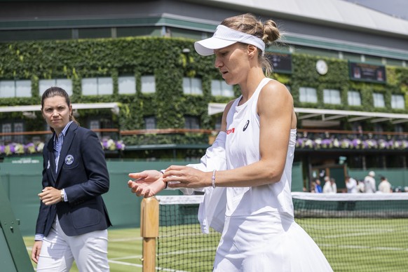 Viktorija Golubic of Switzerland, right, watched by the chair umpire, arrives to the court to her first round match against Iryna Shymanovich of Belarus at the Wimbledon All England Lawn Tennis Champi ...