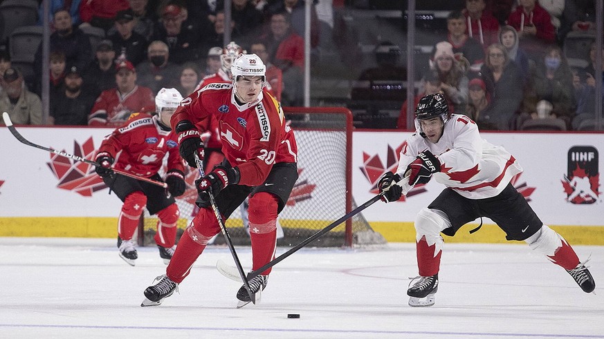 December 19, 2022, Moncton, NB, Canada: Switzerland s Lian Bichsel tries to clear his zone as Canada s Logan Stankoven gives chase during first period IIHF World Junior Hockey Championship pre-tournam ...