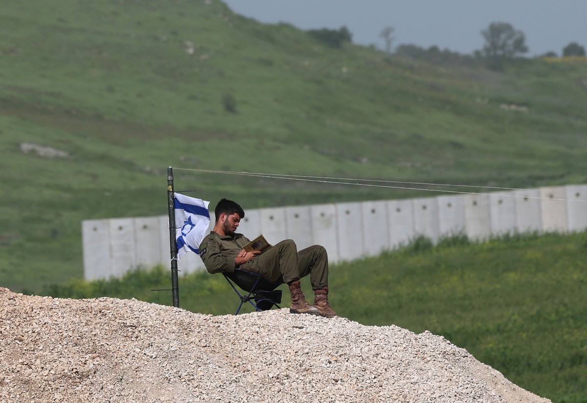 epa12897835 An Israeli soldier reads a book next to an Israeli flag, near the security barrier between Israel and Lebanon near Avivim, Northern Israel, 18 April 2026. Israel and Lebanon have agreed to ...