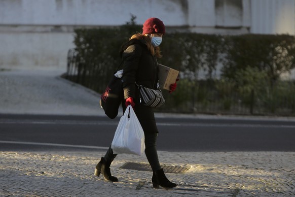 A woman wearing a face mask walks down a street in Lisbon, Monday, Jan. 11, 2021. The COVID-19 pandemic is quickly worsening in Portugal with authorities reporting new daily highs of cases and deaths  ...