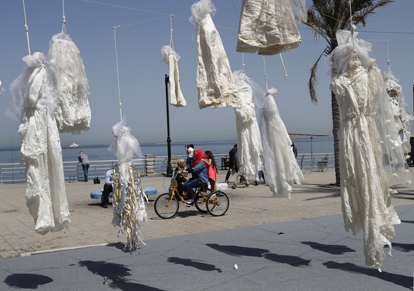 FILE -- In this April 22, 2017 file photo, a veiled woman with her daughter, center, rides a bicycle past white wedding dresses displayed by the Lebanese NGO Abaad, to protest against article 522 in t ...