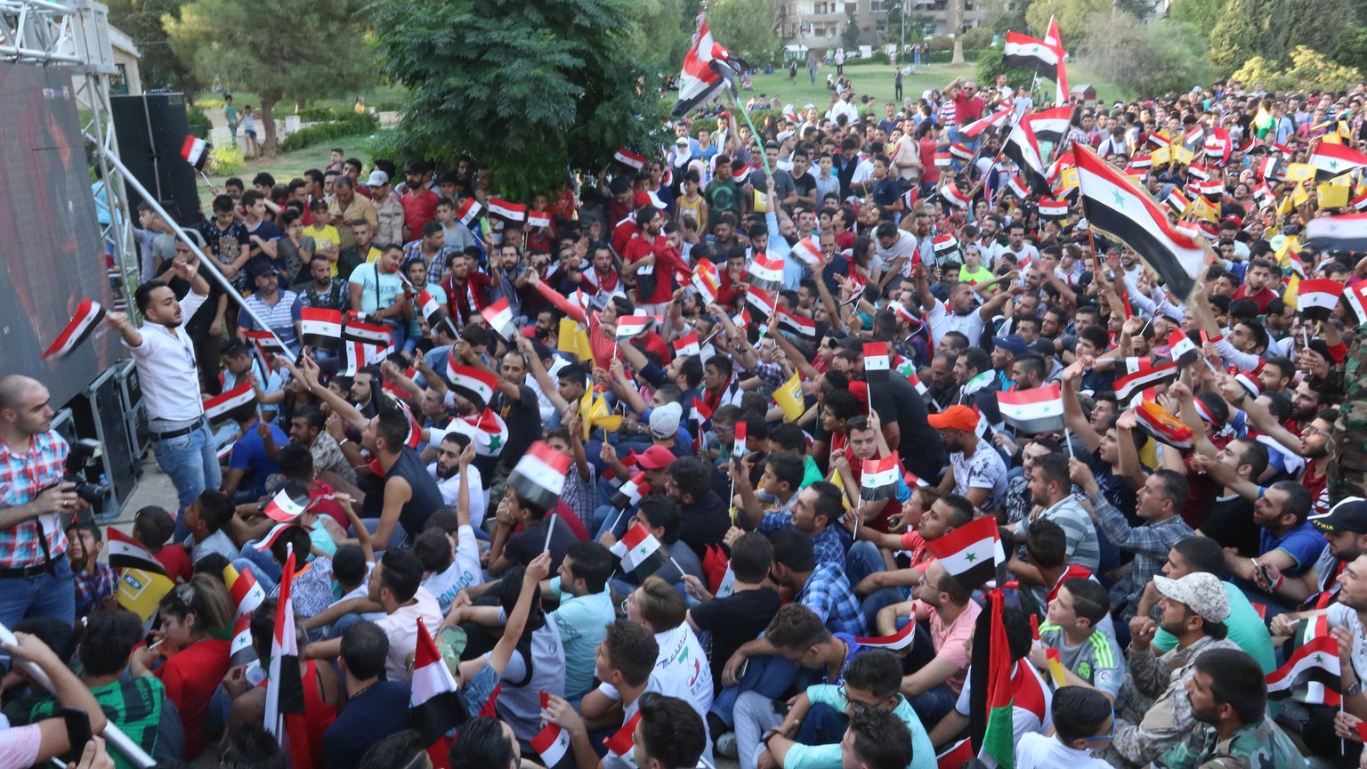 epa06186380 Syrian people watch the FIFA World Cup 2018 qualifying soccer match between Iran and Syria on a huge screen in a park in Damascus, Syria, 05 September 2017. The match between Iran and Syri ...