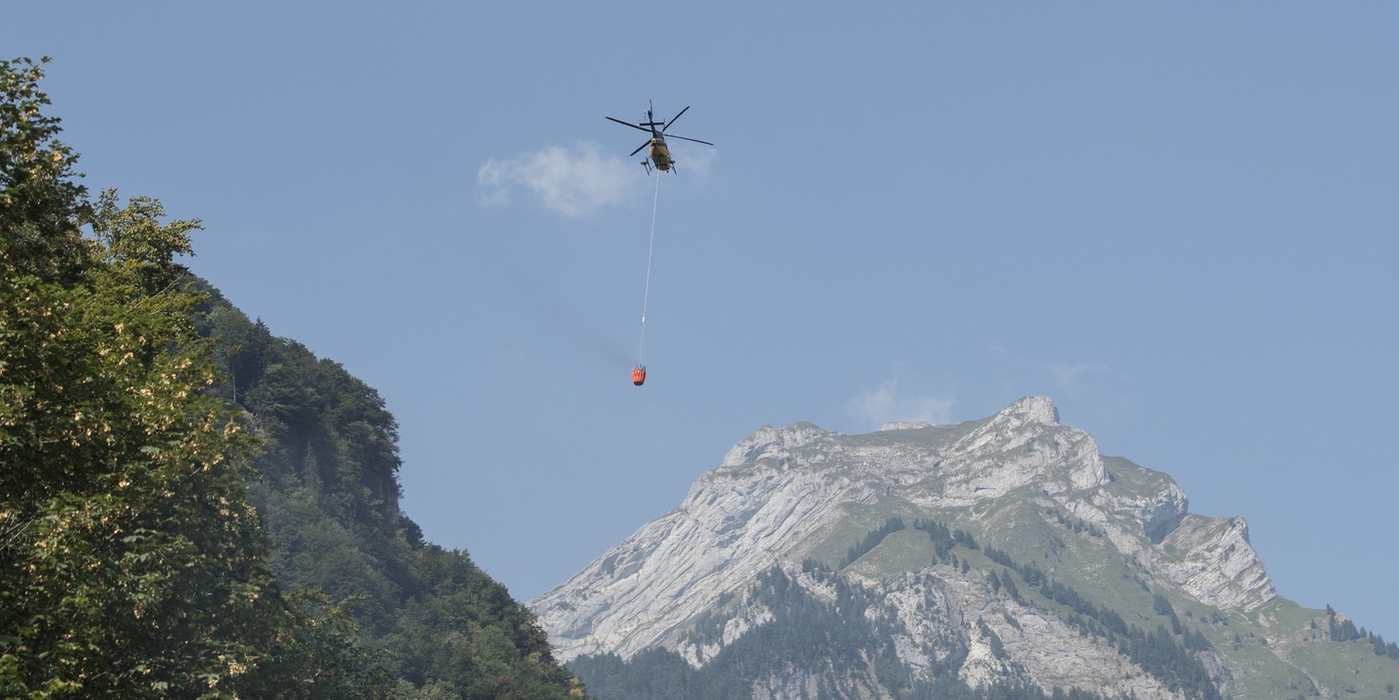 Ein Helikopter transportiert Loeschwasser um den Brandherd nach einem Kleinflugzeugabsturz am Lopper in Hergiswil im Kanton Nidwalden zu loeschen, am Samstag 4. August 2018. (KEYSTONE/Urs Flueeler)