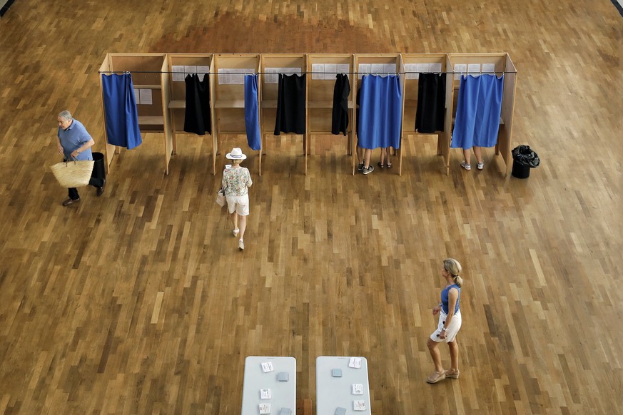 People walk in a polling station before casting their ballots in the first round of parliamentary elections, in Lyon, central France, Sunday, June 11, 2017. French voters are choosing lawmakers in the ...