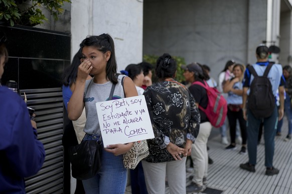 A woman holds a sign with text in Spanish "I'm Betty, a college student and I don't have enough to eat" as she queues with others outside Human Capital Minister Sandra Pet's office...
