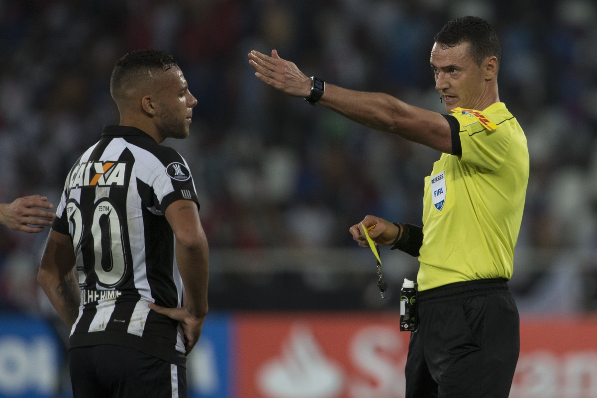 Referee Wilmar Roldan gestures in front of Guilherme, of Brazil's Botafogo, after issuing yellow cards to players of both teams after an argument, during a Copa Libertadores soccer match with Uru ...