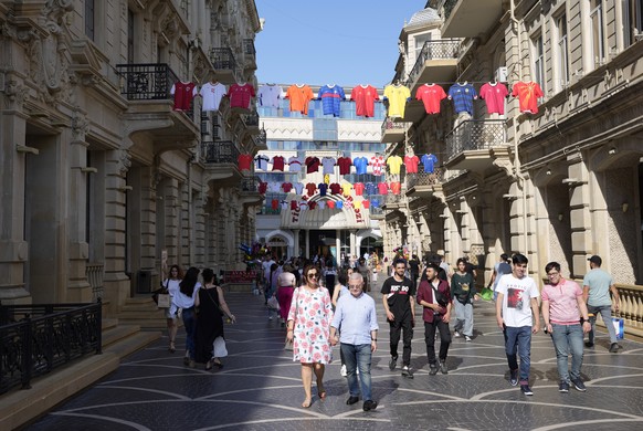 People walk under national teams soccer jerseys advertising the upcoming Euro 2020 soccer championship are displayed in Baku, Azerbaijan, Thursday, June 10, 2021. Euro 2020 gets underway on Friday June 11 and is being played in 11 host cities across 11 countries. The event was delayed by one year after being postponed in 2020 due to the COVID-19 pandemic. (AP Photo/Darko Vojinovic)