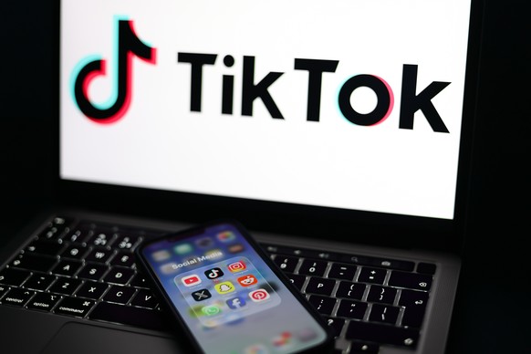 epa12674787 Social media applications displayed on a mobile phone alongside the TikTok logo displayed on a laptop screen in Liverpool, Britain, 23 January 2026. A proposal to ban under-16s from access ...