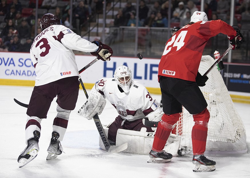 Latvia goaltender Patriks Berzins keeps an eye on the puck as Latvia&#039;s Rihards Simanovics (3) and Switzerland&#039;s Liekit Reichle (24) battle for control during the second period of a IIHF Worl ...