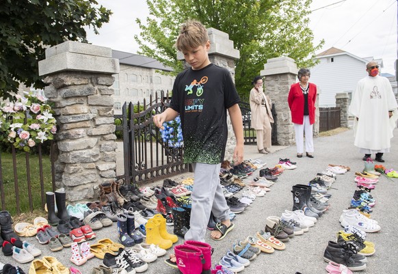 Jamieson Kane puts down tobacco as a tribute to all the victims of the residential school system as he walks amongst children&#039;s shoes outside St. Francis Xavier Church in Kahnawake, Quebec, Sunda ...