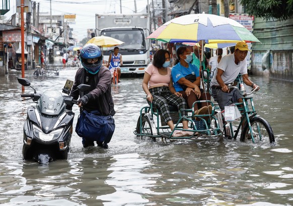 epa10770747 A man (L) pushes his motorcycle through a flooded road as other residents ride a tricycle in Valenzuela City, Metro Manila, Philippines, 27 July 2023. According to the National Disaster Ri ...
