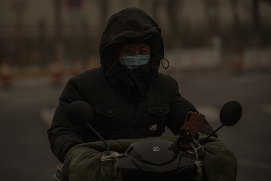 epa09075506 A man wearing a mask rides scooter in the street as the area is hit by sandstorm, in Beijing, China, 15 March 2021. According to the National Meteorological Center, floating sand and dust ...