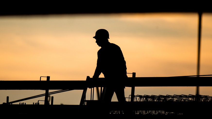 ARCHIV - 31.08.2021, Niedersachsen, Hannover: Die Silhouette eines Bauarbeiters zeichnet sich auf einer Baustelle vor dem verf