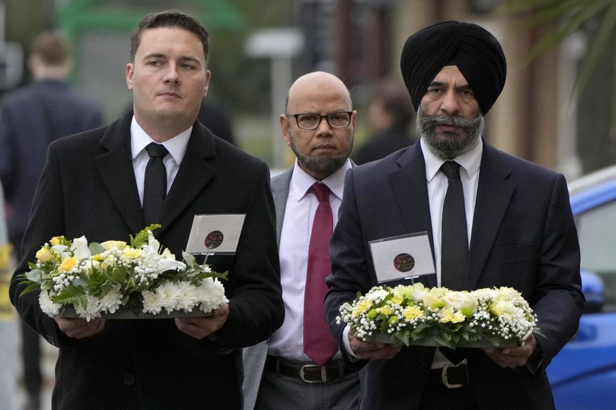 British lawmakers Wes Streeting, left and Jas Athwal, right, leader of Redbridge Council, carry floral tributes to be laid near the Belfairs Methodist Church where British lawmaker David Amess was kil ...