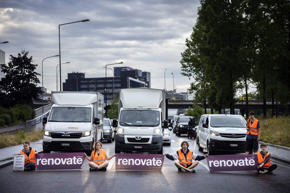 epa10699483 Environmental activists of 'Renovate Switzerland' civil resistance campaign hold banners while sitting down on the road during a roadblock action on the motorway A1 exit in Zueri ...