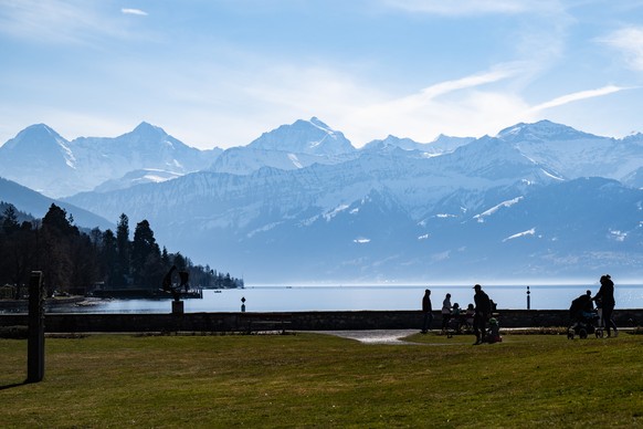 Personen spazieren mit Blick auf Eiger, Moench und Jungfrau im Schadaupark, am Sonntag, 13. Maerz 2022, in Thun. (KEYSTONE/Peter Schneider)