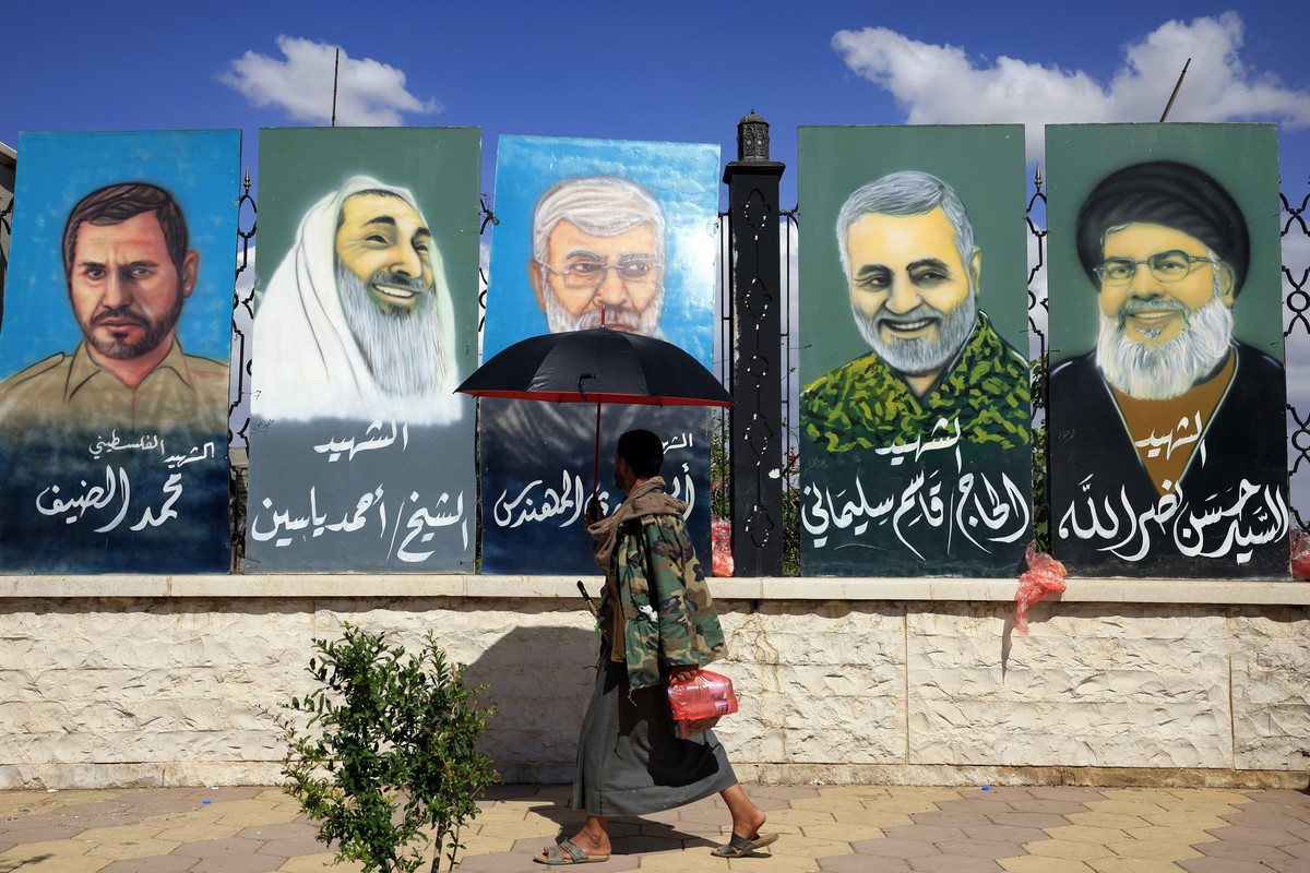 epa12881607 A pedestrian, walking under an umbrella to shield himself from the sun, passes paintings depicting slain military and political figures of Iran-backed Shiite groups, (R-L) late Hezbollah l ...