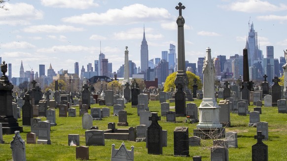 The Empire State building and the Manhattan skyline are seen behind the tombstones at Calvary Cemetery, Saturday, April 11, 2020, in the Maspeth neighborhood of the Queens borough of New York. The U.S ...