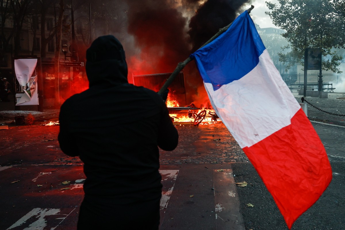 epa13312289 A protester carrying a French flag faces police at Place de la Madeleine during a demonstration against rising living costs and cuts to public services in Paris, France, 17 October 2026. T ...
