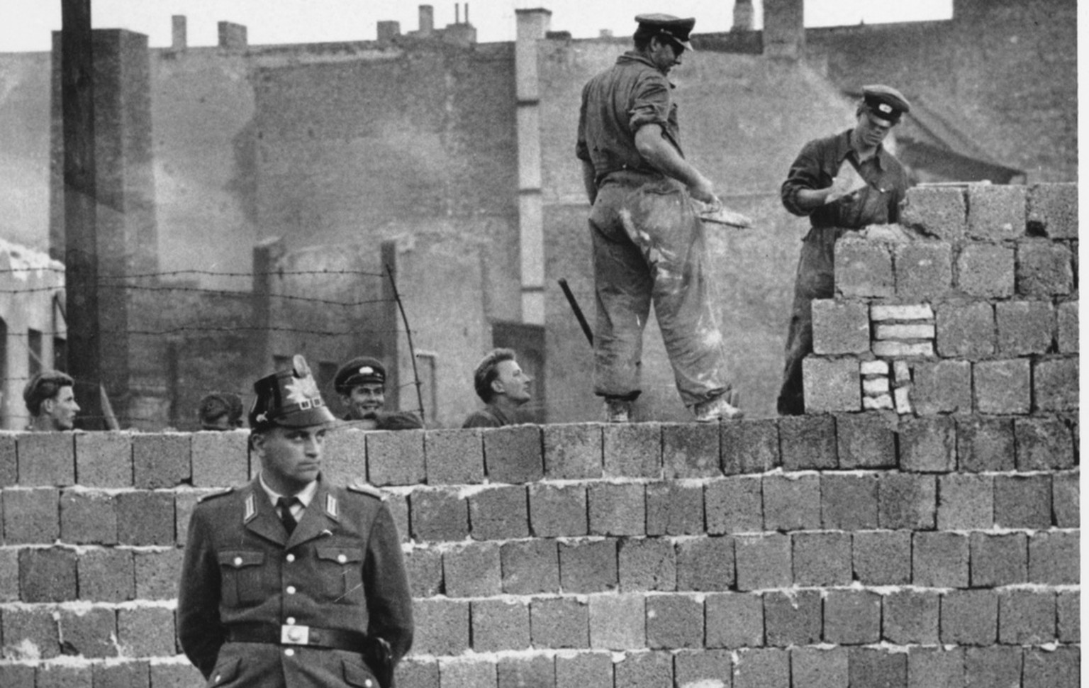 A West Berlin guard stands in front of the concrete wall dividing East and West Berlin at Bernauer Strasse as East Berlin workmen add blocks to the wall to increase the height of the barrier, Oct. 7,  ...