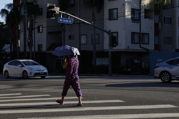 epa11585689 A person crosses an intersection holding an umbrella for shade in Los Angeles, California, USA, 04 September 2024. Excessive-heat warnings are in effect through 06 September for much of So ...