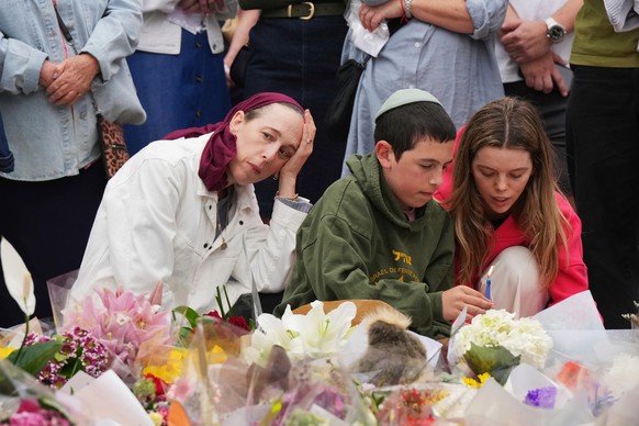People react during a menorah lighting ceremony at a floral memorial for victims of Sunday's shooting, at the Bondi Pavilion on Bondi Beach on Tuesday, Dec. 16, 2025, in Sydney, Australia. (AP Ph ...