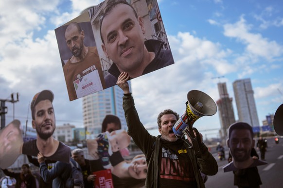FILE - A demonstrator wave photos of freed Israeli hostage Eli Sharabi before and after his captivity blocks a highway during a protest demanding all hostages release from Hamas captivity, in Tel Aviv ...