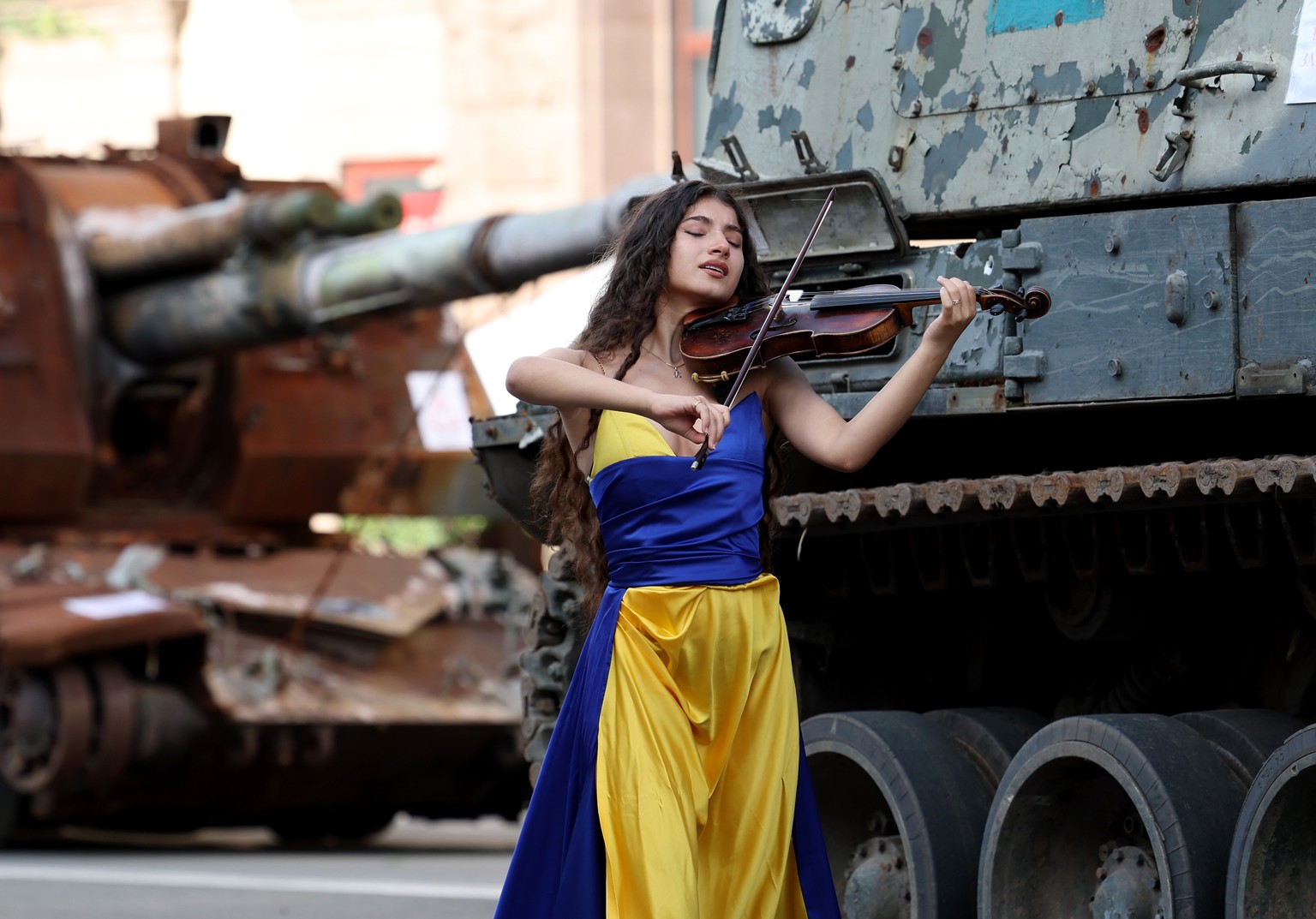 epa10815065 A woman dressed in the colors of the Ukrainian national flag takes part in a music video as she walks past damaged Russian armored military vehicles that were seized by the Ukrainian army  ...