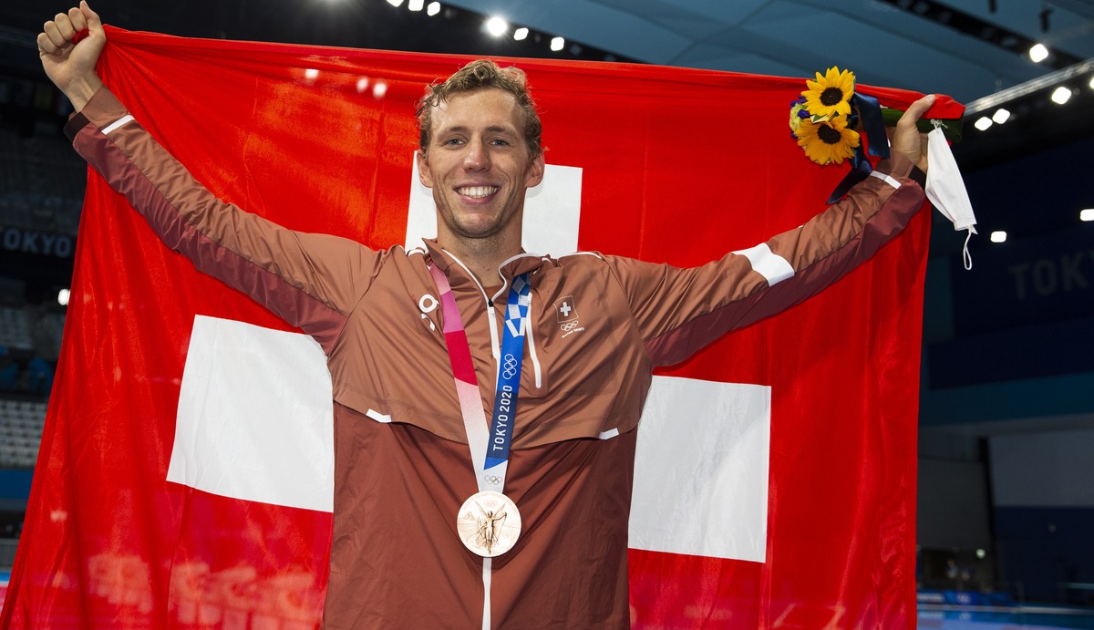 epa09378091 Jeremy Desplanches of Switzerland poses with his Bronze medal and a Swiss flag after finishing third in the men's 200m Individual Medley Final during the Swimming events of the Tokyo  ...
