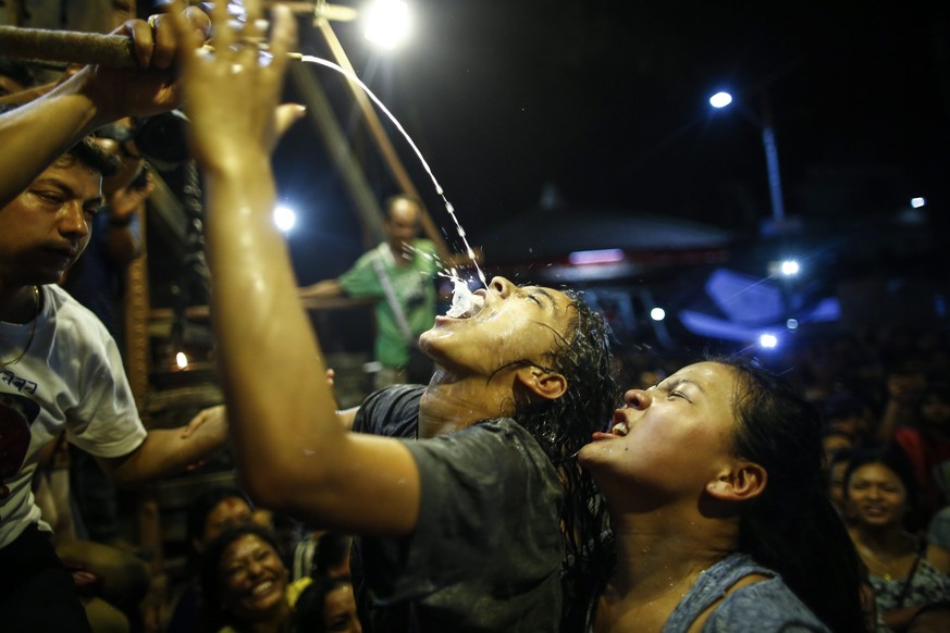epa05544818 Nepalese women and young girls struggle to drink homemade alcohol poured through a pipe sticking out of the mouth of Swet Bhairab, a god of Power, during the Indra Jatra festival at Basant ...