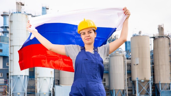 Positive young female worker in helmet waving national flag of Russia while standing in front of big tanks at refinery factory Model Released Property Released xkwx chemical, factory, woman, flag, Rus ...