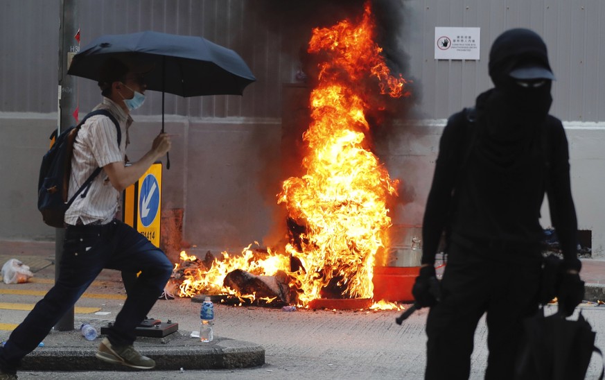 A black-clad protestor stands by flames rising from a fire in Hong Kong, Tuesday, Oct. 1, 2019. A Hong Kong police official says a pro-democracy protester was shot when an officer opened fire with his ...