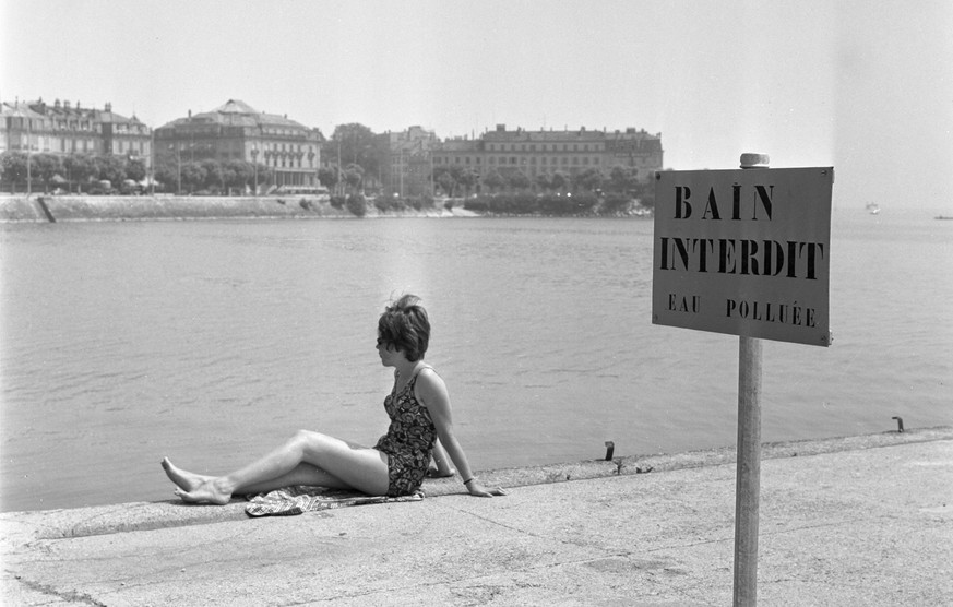 Eine Badeverbotstafel und eine Frau im Badekleid am verschmutzten Neuenburgersee, aufgenommen im Sommer 1964. (KEYSTONE/Str)