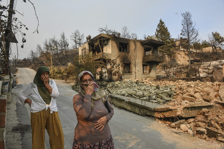 People walk in wildfire-destroyed Kalemli village near Manavgat, Antalya, Turkey, Monday, Aug. 2, 2021. For the sixth straight day, Turkish firefighters were battling Monday to control the blazes tear ...