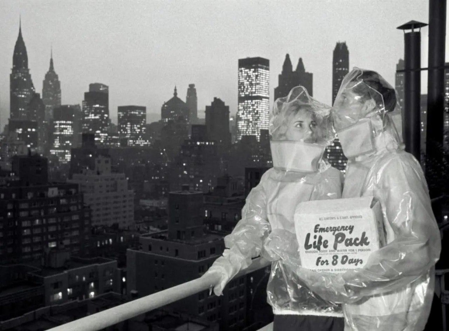 A New York couple modeling Cold War fallout suits and an 8-day survival kit, 1961