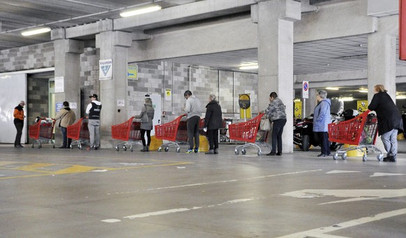 epa08288388 Customers keep a safety distance between each other as they wait in a long line to buy goods at a supermarket in the alpine city of Aosta, northwestern Italy, 12 March 2020. All establishm ...