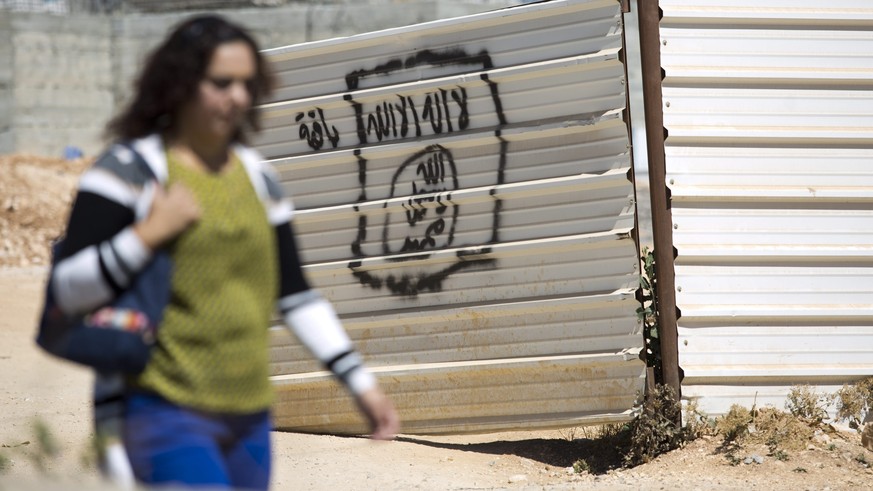 epa04831951 A Palestinian walks past a graffiti supposed to depict the flag of the jihadist terror group referring to itself as the 'Islamic State' in the Arab neighborhood of Beit Hanina in ...