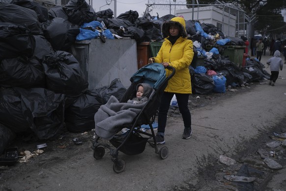 A migrant woman passes with her baby in front of garbage dumped outside the Moria refugee camp on the northeastern Aegean island of Lesbos, Greece, on Tuesday, Jan. 21, 2020. Some businesses and publi ...