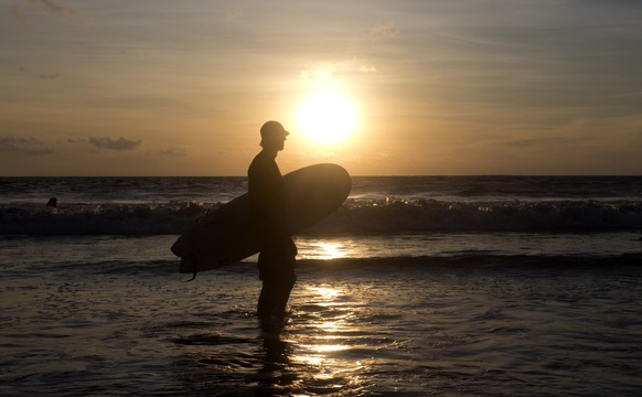 A man carries his surfboard walks at Kuta beach during the sunset in Bali, Indonesia on Tuesday, Feb. 16, 2021. (AP Photo/Firdia Lisnawati)