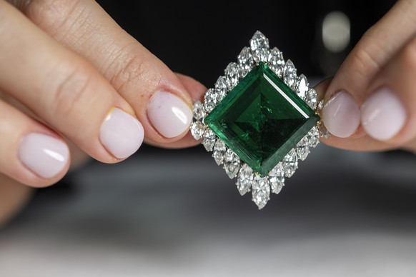 A Christie&#039;s employee displays the Aga Khan Emerald. A Cartier emerald and diamond brooch, 1960. Square-shaped emerald of 37.00 carats, marquise-shaped diamonds, platinum and 18k yellow gold. 4.9 ...