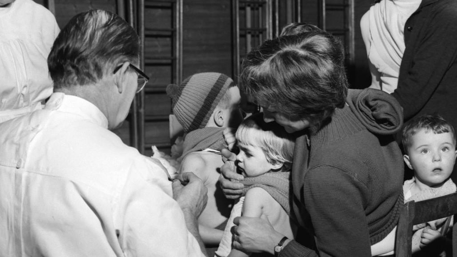 Bei einer freiwilligen Impfaktion der Bevoelkerung von Schaffhausen am 8. Januar 1962 impft ein Arzt ein Kind in den entbloessten Oberarm, waehrend eine Mutter mit ihren Kindern auf die Impfung warten ...