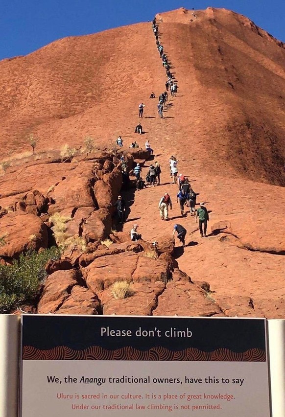 Schild im Vordergrund: «Wir, die Anangu, traditionelle Eigentümer, haben Folgendes zu sagen: Uluru (Kolonialname Ayers Rock, Anm. d. Red.) ist heilig in unserer Kultur. Es ist ein Ort grossen Wissens. ...