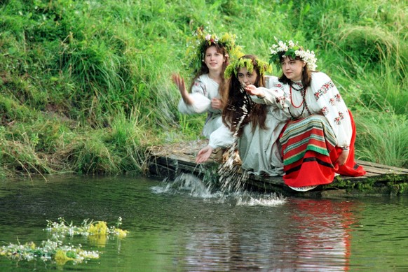 Three Ukrainian girls dressed in traditional folk costumes let down the ritual garlands on a water during the Midsummer Night celebration in Kiev, Ukraine, dawn Tuesday, July 7, 1998.  Ukrainian girls beleive that ages-old ceremony would help them to find the fiances. The pagan Slav festival is still celebrated in Ukraine. (AP Photo/Efrem Lukatsky)