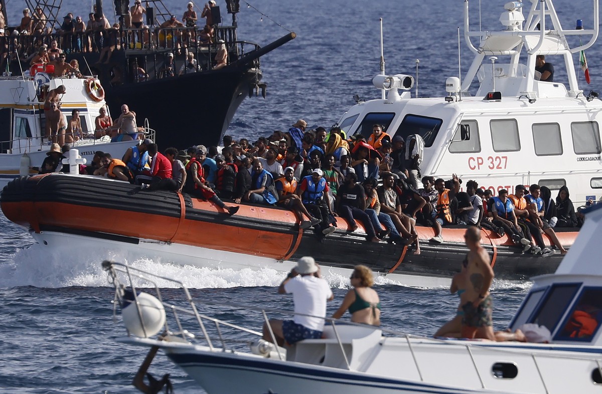 An Italian Coast Guard boat carries migrants as tourists on boat, foreground, watch, near the port of the Sicilian island of Lampedusa, southern Italy, Monday, Sept. 18, 2023. The Italian Cabinet met  ...