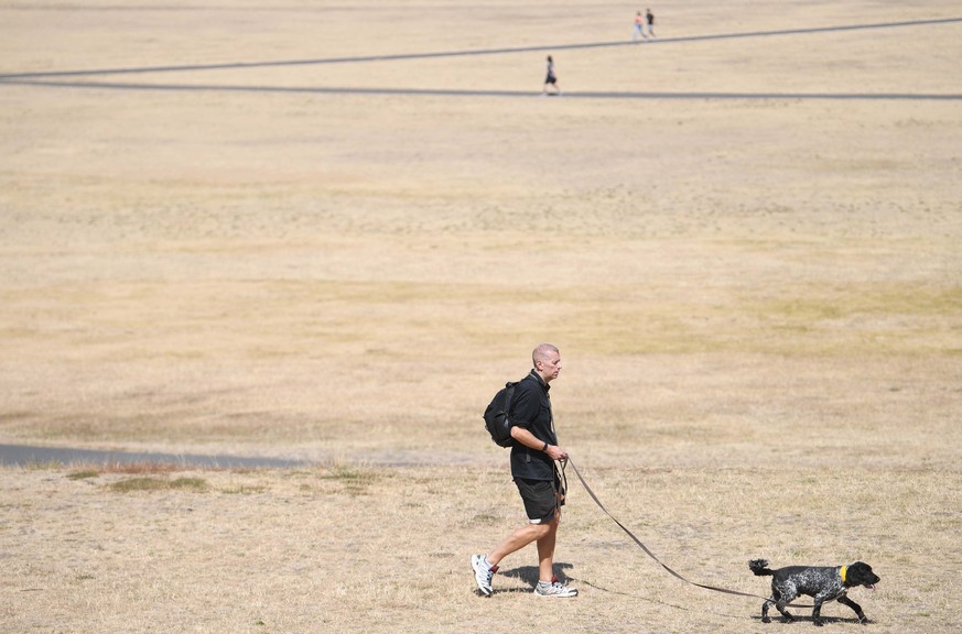 epa10108886 People walk on parched ground in Greenwich Park in London, Britain, 06 August 2022. Southern England has experienced the driest July since records began. With another heatwave expected in  ...
