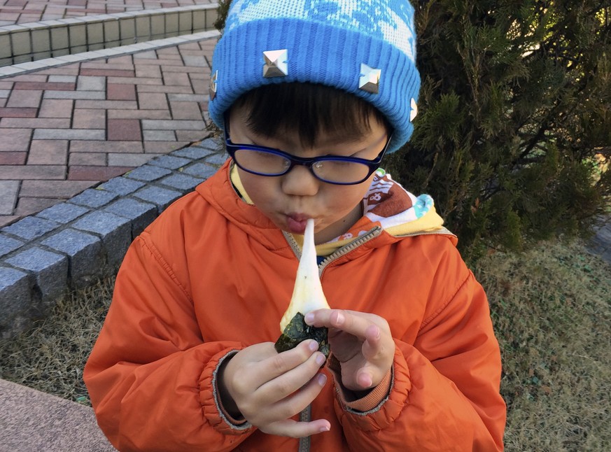 In this Saturday, Dec. 13, 2014 photo, a boy eats a freshly pounded rice cake, or &quot;mochi,&quot; wrapped in a sheet of seasoned laver, or &quot;nori,&quot; at a park during a rice pounding gatheri ...