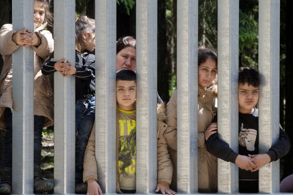 Members of a group of some 30 migrants seeking asylum are seen in Bialowieza, Poland, on Sunday, 28 May 2023 across a wall that Poland has built on its border with Belarus to stop massive migrant pres ...